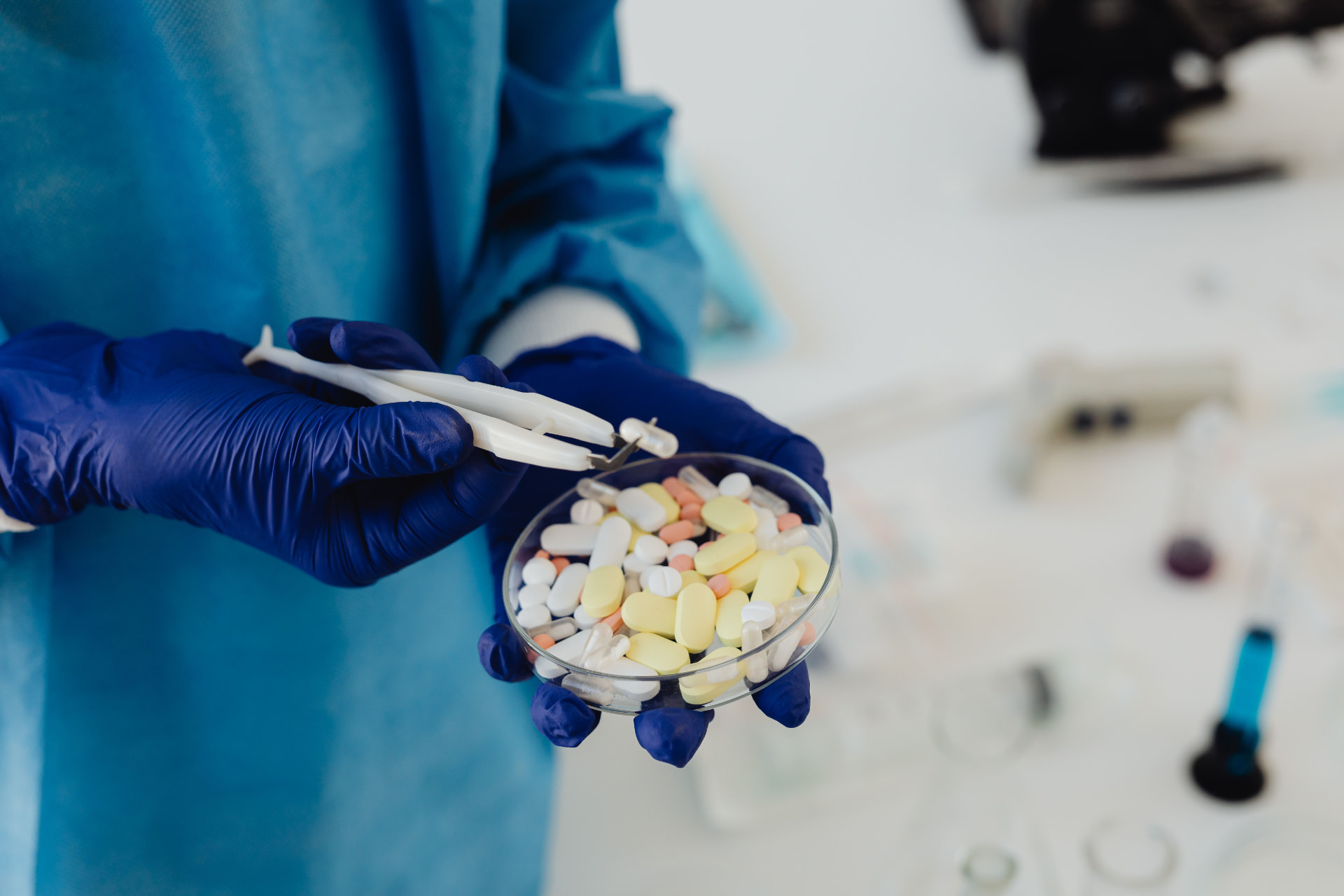 Lab technician holding a petri dish of medication tablets with tweezers